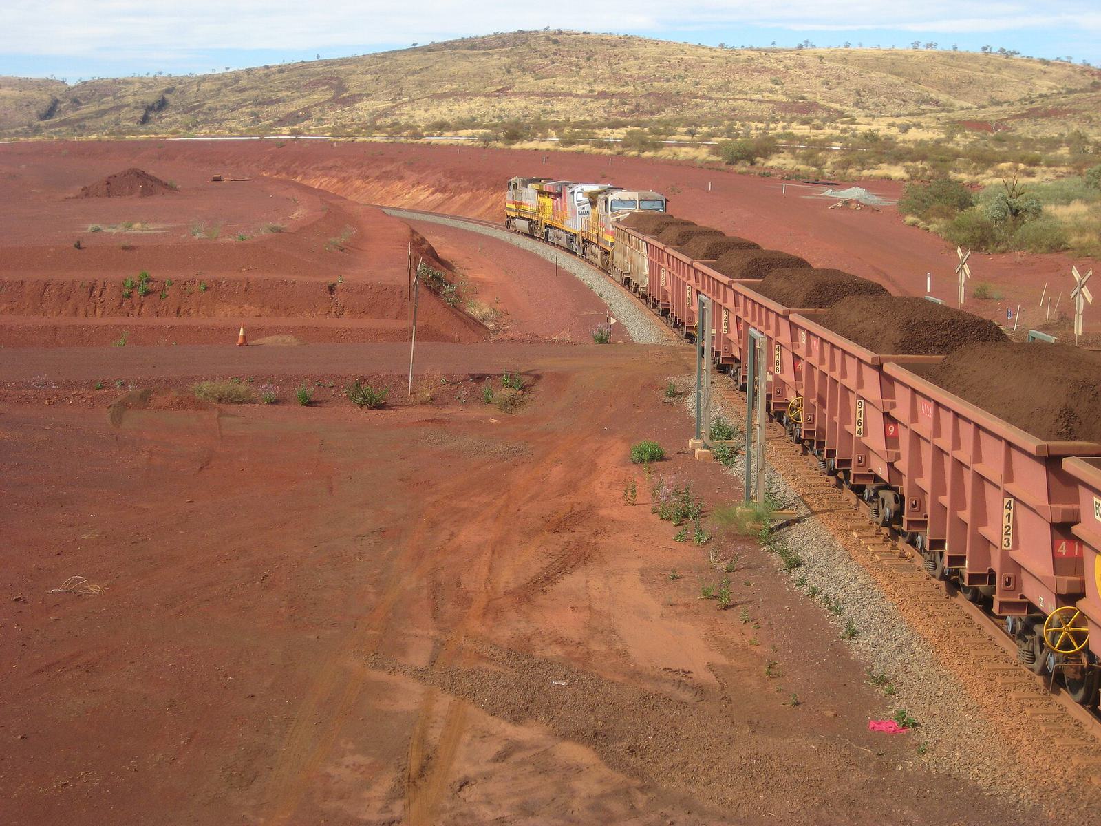 A long train of ore wagons on red earth in the Pilbara